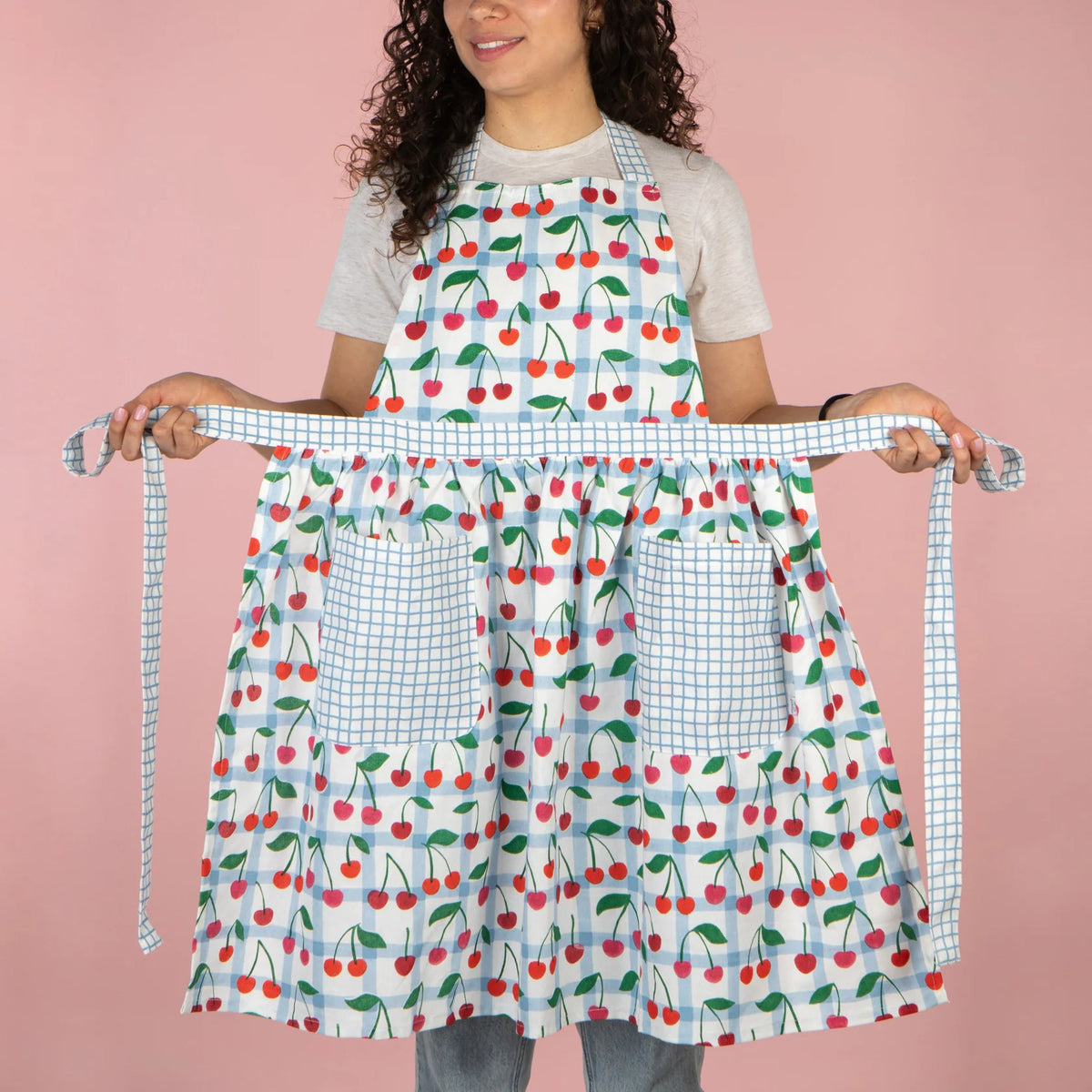 Person wearing a colorful apron with cherry pattern on a pink background