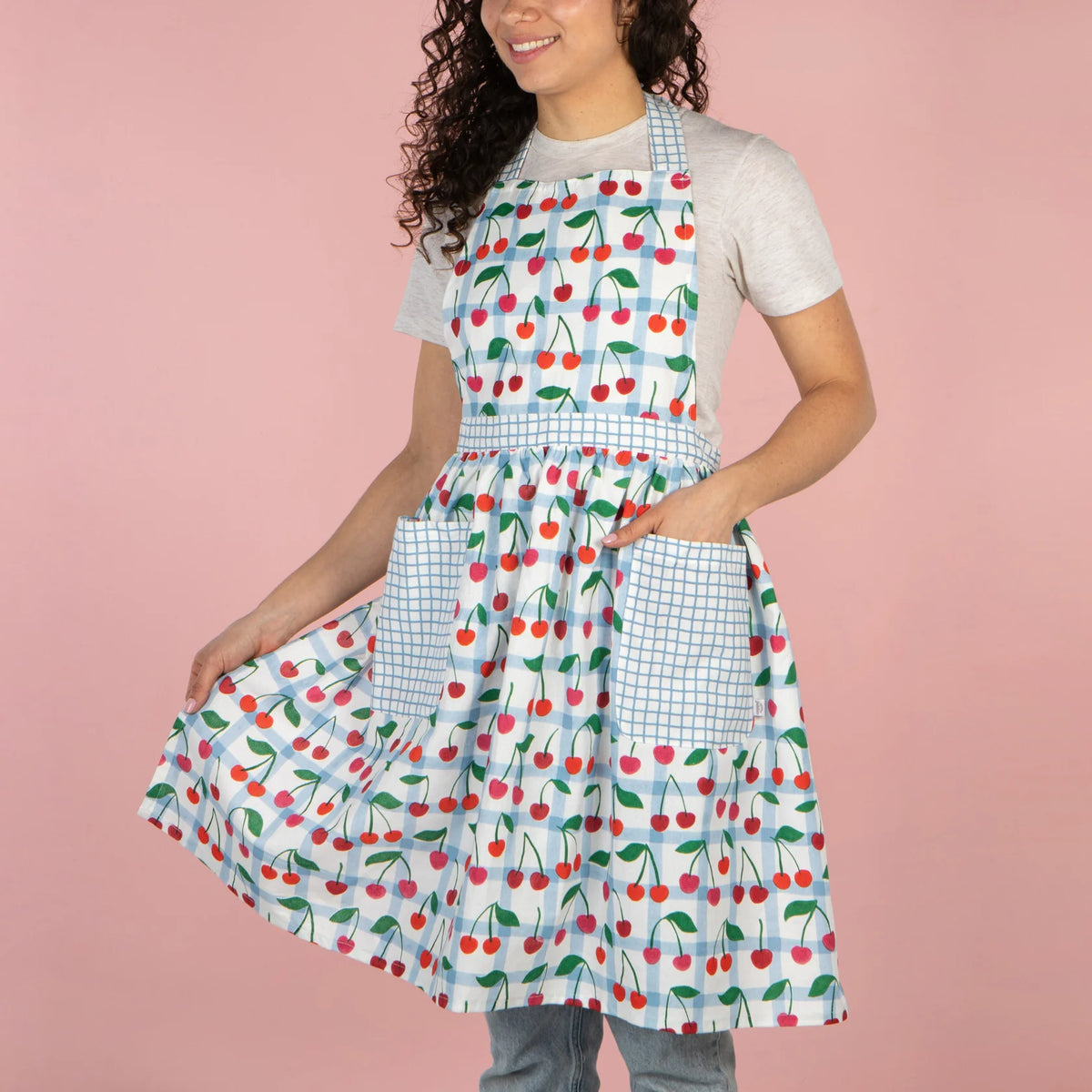 Person wearing a colorful apron with cherry pattern on a pink background