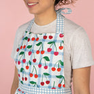 Person wearing a colorful apron with cherry pattern on a pink background